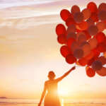 Woman walking into sunset with red balloons