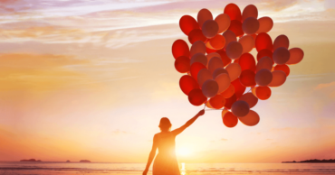 Woman walking into sunset with red balloons